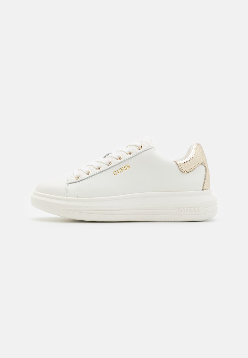 Valged nahk sneakers kuldsete aktsentidega, ümmargune ninaosa, nööridega disain ja tekstureeritud kuldne konts. Omab kaubamärki "GUESS" kuldsete tähtedega.