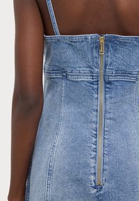 Denimkjole med en tettsittende design, glidelåslukking bak, justerbare tynne stropper og en lys blåvasket tekstur.