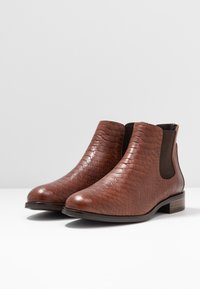 Brązowe skórzane botki za kostkę z fakturowanym wzorem węża, elastycznymi panelami bocznymi oraz płaskim obcasem. Gładkie wykończenie z eleganckim designem.