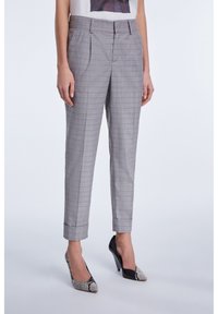 Pantalons à carreaux gris à taille haute, avec des plis et des jambes fuselées, assortis à des escarpins à motifs noir et blanc.