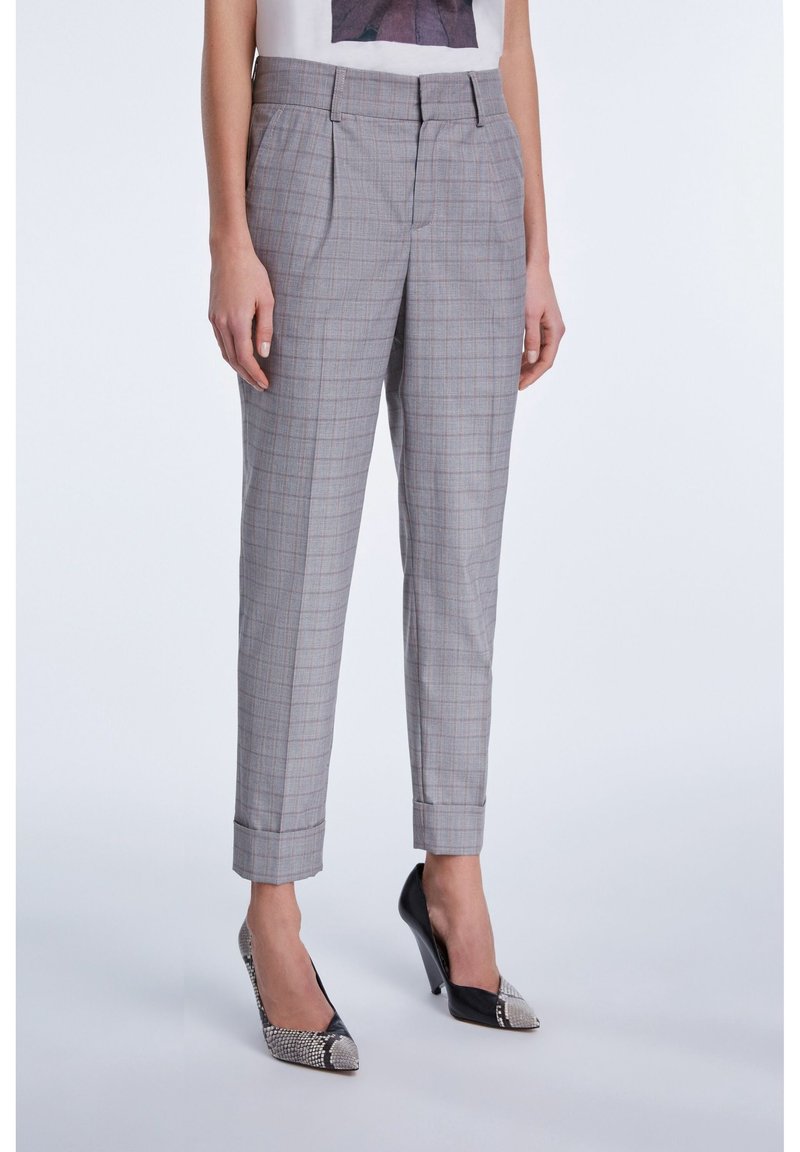 Pantalons à carreaux gris à taille haute, avec des plis et des jambes fuselées, assortis à des escarpins à motifs noir et blanc.