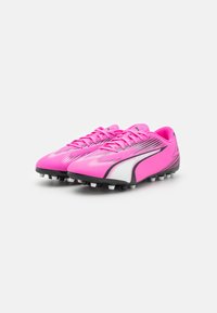 Scarpe da calcio sintetiche rosa con accenti neri, caratterizzate da un design aerodinamico, parte superiore testurizzata e suola bianca con tacchetti per una migliore aderenza.
