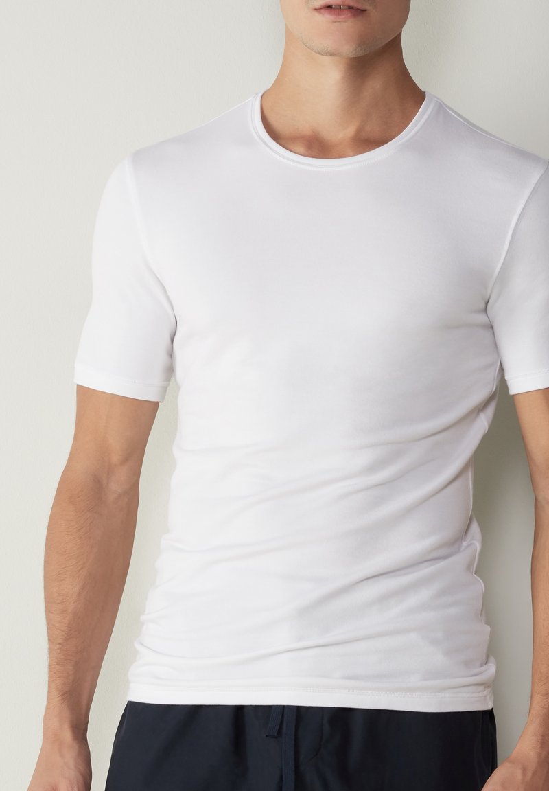 T-shirt blanc à manches courtes en coton léger. Il présente un col rond et une texture lisse, avec une coupe ajustée et des coutures minimales.