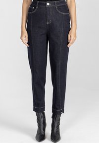 Ciemnoniebieskie dżinsy o prostym kroju z złotymi szwami, pięcioma kieszeniami i skróconym dołem, w połączeniu z czarnymi botkami na obcasie.