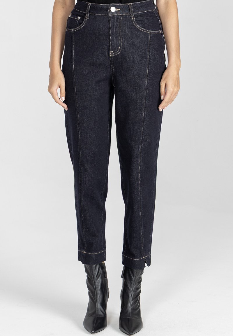 Ciemnoniebieskie dżinsy o prostym kroju z złotymi szwami, pięcioma kieszeniami i skróconym dołem, w połączeniu z czarnymi botkami na obcasie.