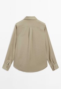 Camicia beige a maniche lunghe con colletto classico, piega sul retro, polsini con bottone e orlo curvo, realizzata in tessuto liscio.