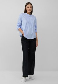 Blusa azzurro chiaro a maniche lunghe con righe bianche verticali, pieghe sul colletto e bottoni decorativi. Abbinata a pantaloni neri a gamba larga e sneakers bianche.