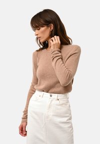 Hellbraunes Strickpullover mit langen Ärmeln, rundem Ausschnitt, kombiniert mit einem weißen Denim-Rock. Weiche Textur, lässige Passform.