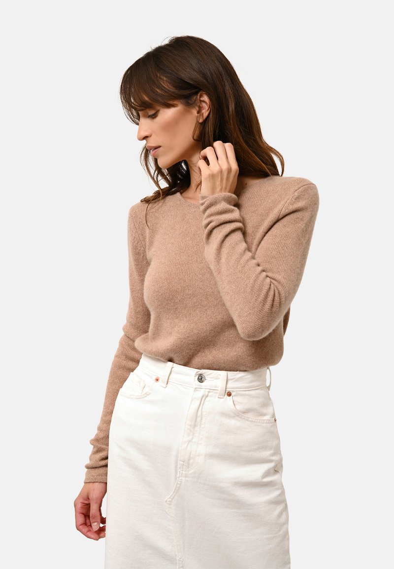Hellbraunes Strickpullover mit langen Ärmeln, rundem Ausschnitt, kombiniert mit einem weißen Denim-Rock. Weiche Textur, lässige Passform.