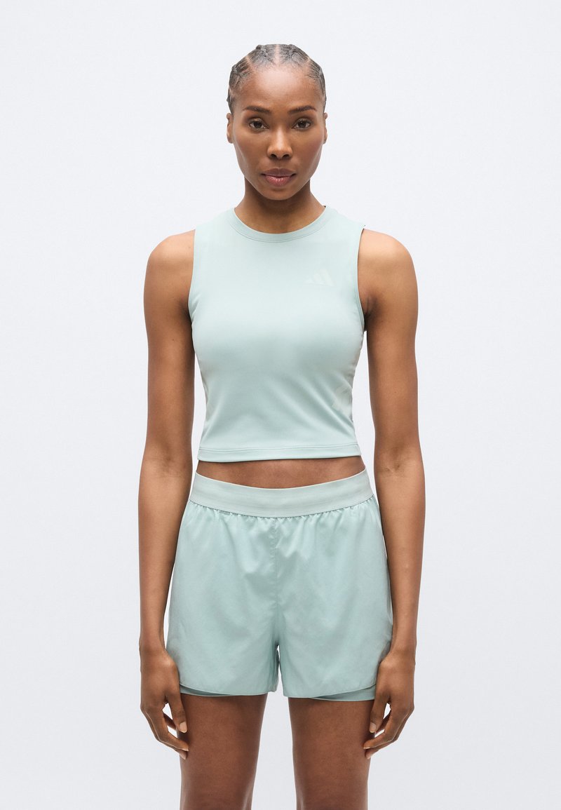 Haut de sport court vert clair avec un col rond, associé à un short assorti. Les deux articles sont fabriqués en tissu lisse et léger.