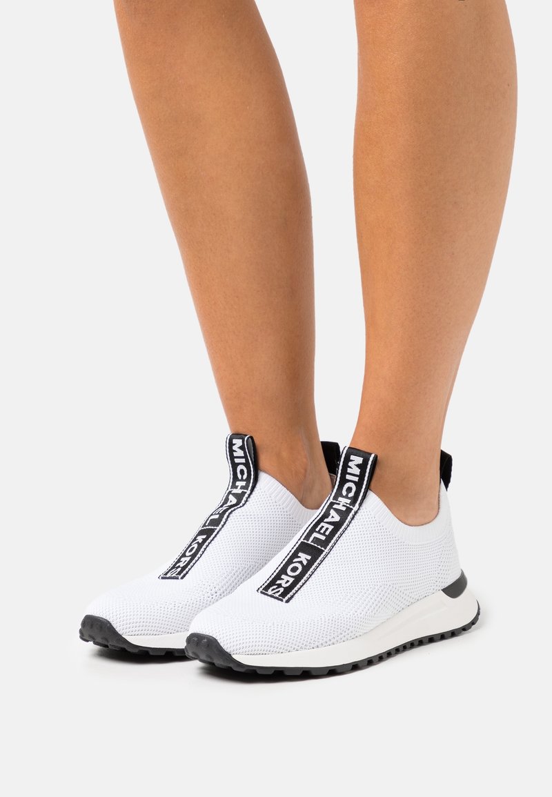 Weiße Slip-On-Sneakers mit einem Obermaterial aus Mesh, ausgestattet mit einem schwarzen Logo-Riemen und einer strukturierten Gummisohle. Leichtes und flexibles Design.