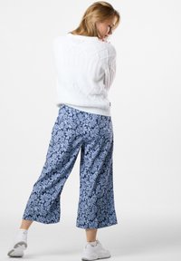 Vit stickad tröja med diamantmönster, i kombination med marinblå vida byxor med blommönster. Modell som bär vita sneakers.