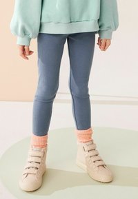 Kék bordás leggings egy mentazöld, oversized pulóverrel párosítva. Világos rózsaszín, mintás zoknik és bézs magas szárú cipők pántokkal.