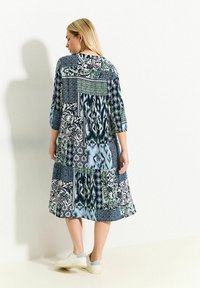 Vestido de patchwork multicolor con una mezcla de patrones florales y geométricos; presenta mangas largas y un ajuste holgado, combinado con zapatillas blancas.