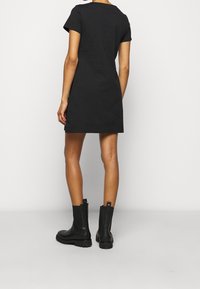 Abito corto nero a maniche corte con taglio dritto e scollo rotondo. Indossato con stivaletti neri impermeabili alla caviglia con suola testurizzata.