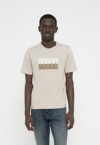 Μπεζ βαμβακερό t-shirt με κοντά μανίκια, με ορθογώνιο καφέ και λευκό λογότυπο εκτυπωμένο μπροστά που αναγράφει "JACK & JONES".