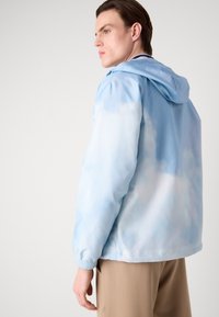 Kerge kapuutsiga jakk, millel on gradientne sinine värv, mis meenutab pilvi, elastsed mansetid ja lõdvem lõige.