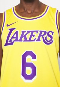 Gul baskettröja med lila detaljer. "LAKERS" tryckt med stora bokstäver. Nummer "6" i lila nedanför. Tillverkad av meshtyg.