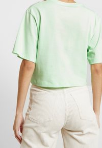 Zkrácené tričko světle zelené barvy z měkké látky s krátkými rukávy, kombinované s béžovými manžestrovými kalhotami s vysokým pasem a žebrovanou texturou.