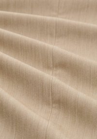 Tessuto beige con sottili righe verticali e morbide pieghe che evidenziano una cucitura centrale che attraversa il centro.