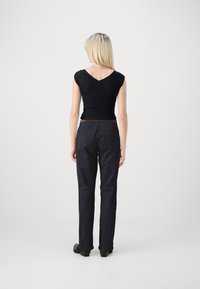 Μαύρη εφαρμοστή μπλούζα με κοντά μανίκια και V-λαιμόκοψη, σε συνδυασμό με σκούρες μπλε παντελόνες καμπάνα. Λείος υφασμάτινος, απλός σχεδιασμός, χωρίς ορατά μοτίβα.