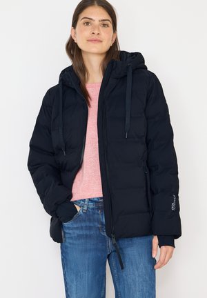Navy padded jacket with a hood, featuring elastic cuffs, front zipper, and drawstrings. Worn over a pink sweater and blue jeans.