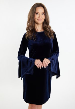 Robe en velours bleu marine avec des manches évasées, un col rond et une texture douce. Le tissu a l'air lisse et légèrement réfléchissant.