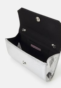 Srebrna metaliczna kopertówka o teksturowanej powierzchni, z czarną podszewką i zapięciem na magnes. Wewnątrz znajduje się kieszonka na karty.