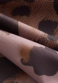 Texturovaná látka v odstínech růžové a hnědé s vzorem leopardího potisku, obsahující tmavé, nepravidelné tvary a jemný, tkaný vzhled.