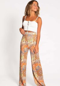 Top corto blanco con tirantes finos y detalle de lazo; pantalones de pierna ancha con un vibrante patrón floral en tonos naranjas, azules y amarillos.