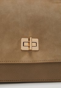 Sac à main beige avec partie supérieure en daim et partie inférieure en cuir grainé, doté d'une fermeture à tourniquet en métal doré rectangulaire au centre.