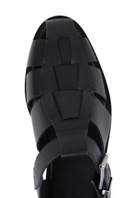 Sandale en cuir noir avec un design à bout ouvert, présentant des sangles verticales et horizontales, et une boucle en métal argenté réglable. Semelle plate.