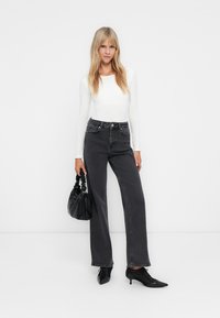 Jeans negros de tiro alto combinados con una blusa blanca de manga larga. Accesorios con un bolso negro y tacones negros de punta. Textura suave.