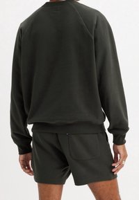 Tmavě zelená bavlněná mikina s kulatým výstřihem a žebrovanými manžetami, doplněná o odpovídající šortky se zadní kapsou. Hladká textura.