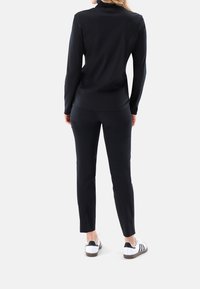 Schwarzes Langarmoberteil mit hohem Kragen, kombiniert mit schwarzen Slim-Fit-Hosen und weißen Sportschuhen mit schwarzen Streifen und braunen Sohlen.