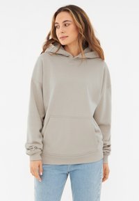 Hanorac gri deschis cu un buzunar frontal mare, glugă cu șnur, manșete ribbate și un croi lejer, asortat cu blugi albaștri. Textură netedă.