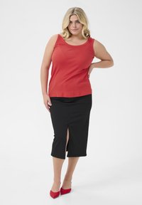 Red sleeveless top paired with a black midi skirt featuring a front slit; model wearing red pointed heels, plain background.