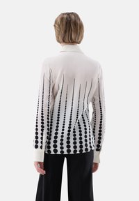 Blusa a maniche lunghe in tessuto bianco con un motivo a gradiente di pois neri, con colletto a punta e polsini con bottone.
