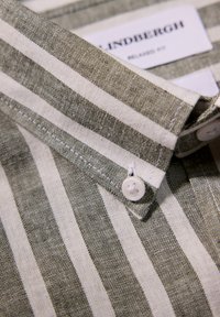 Grøn- og hvidstribet skjortedetalje med en button-down krave, struktureret stof og en hvid knap med et krydsmønster.