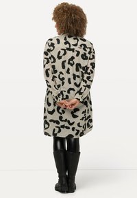 Beige en zwarte shirtjurk met luipaardprint, voorzien van een kraag, knopen aan de achterkant en lange mouwen. Gemaakt met zwarte, leren look leggings en laarzen.