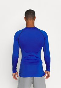 Langarm-Athletic-Shirt in leuchtendem Blau, mit einer taillierten Passform, glatter Textur und kontrastierenden schwarzen Nähten entlang der Schultern und Seiten.