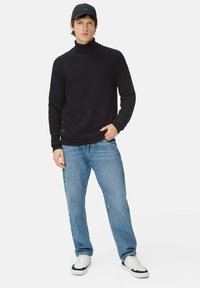 Navyfarbener Strickrollkragenpullover mit strukturiertem Muster, kombiniert mit hellblauen Jeans und weißen Sneakern. Eine Kappe mit flachem Schirm rundet den Look ab.