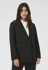 Juodas švarkas, pagamintas iš lygios medžiagos, su vienu sagos uždarymu, notch tipo atlapais ir dviem priekinėmis kišenėmis. Ilgos rankovės ir pritaikytas siluetas.