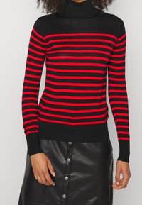 Maglione a collo alto nero con audaci strisce orizzontali rosse. Texture morbida. Presenta maniche lunghe e polsini e orlo a coste.