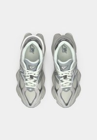 Γκρι αθλητικά παπούτσια με άνω μέρος από διχτυωτό υλικό, επαλείψεις υφών και ανακλαστικές λεπτομέρειες. Διαθέτουν μαξιλαρωτή σόλα και λευκές κορδόνες.
