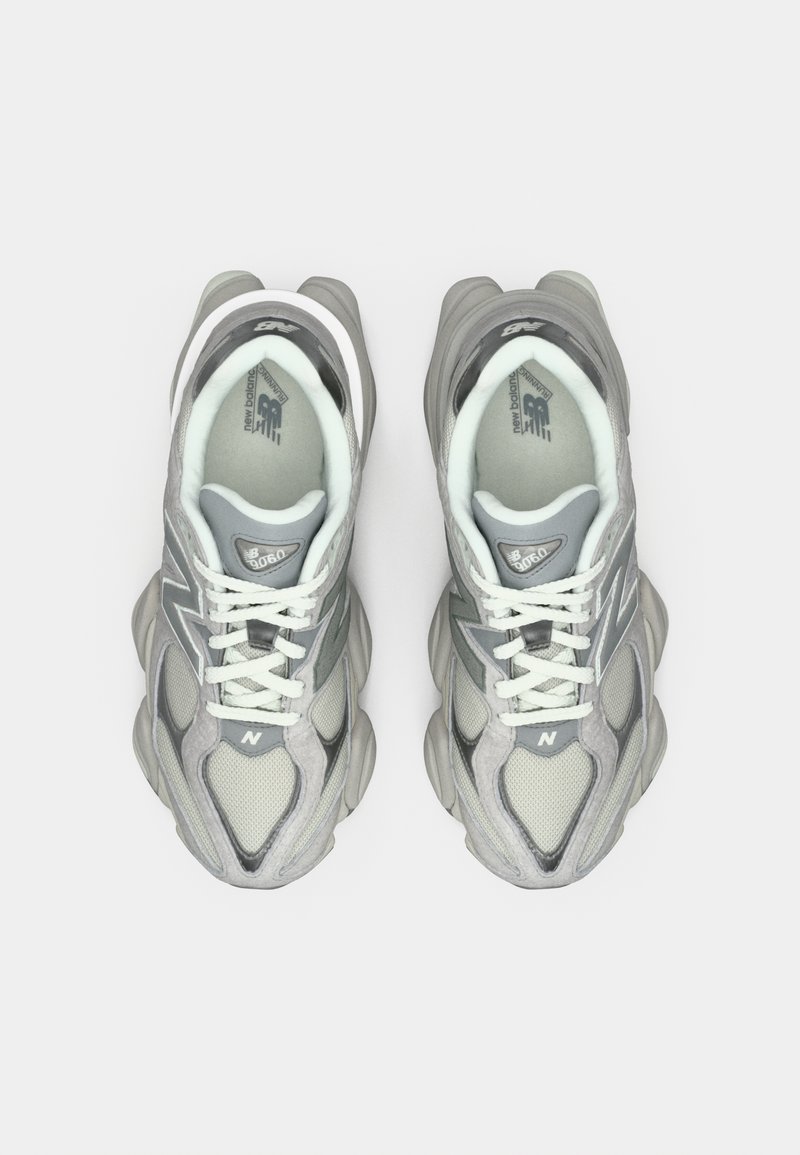 Graue Sportschuhe mit einem Mesh-Obermaterial, schichteten Texturen und reflektierenden Akzenten. Mit einer gepolsterten Sohle und weißen Schnürsenkeln.