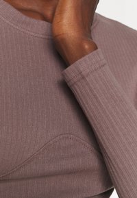 Tailliertes Langarmoberteil in Mauve aus geripptem Stoff mit strukturiertem Detail; mit einem runden Halsauschnitt und enganliegenden Ärmeln.