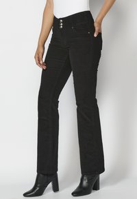 Pantalones de mezclilla negros acampanados con cintura alta, que presentan tres botones plateados, bolsillos frontales y detalles de costura a lo largo de las piernas.