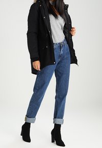 Czarna parka z futrzanym kapturem, szara koszula, niebieskie dżinsy o wysokim stanie i czarne botki na obcasie. Casualowy miejski zestaw z podwiniętymi rękawami.