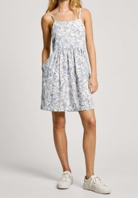 Floral print dress with spaghetti straps, gathered waist, and side pockets. Light blue and white color scheme with a flowing design.